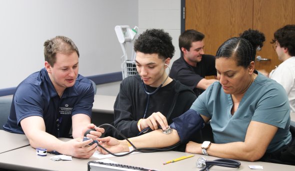 In a classroom, a nursing student is demonstrating how to take blood pressure on a patient.