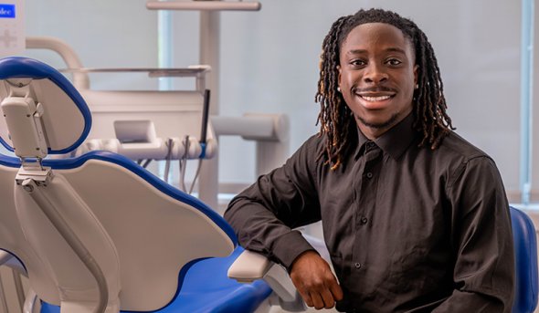 Benjamin Quansah sits next to dental chair in clinic.