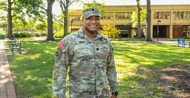 A man stands outside in front of a building and some trees. 