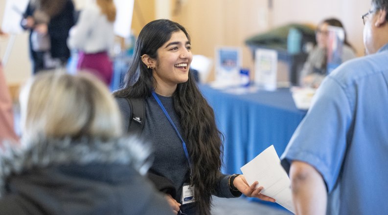 A student smiling and talking to people at an event.