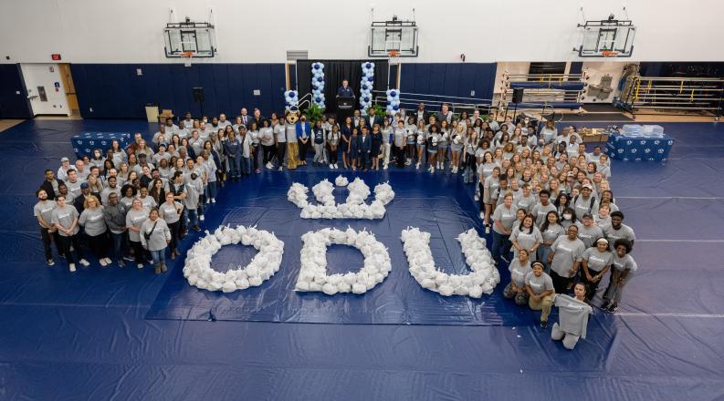 Faculty, staff, and students who participated int he event stand around the packed bags of foos which are arranged to make the ODU logo on the floor.
