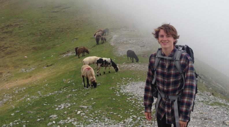 student hiking with a background of green fields and sheep