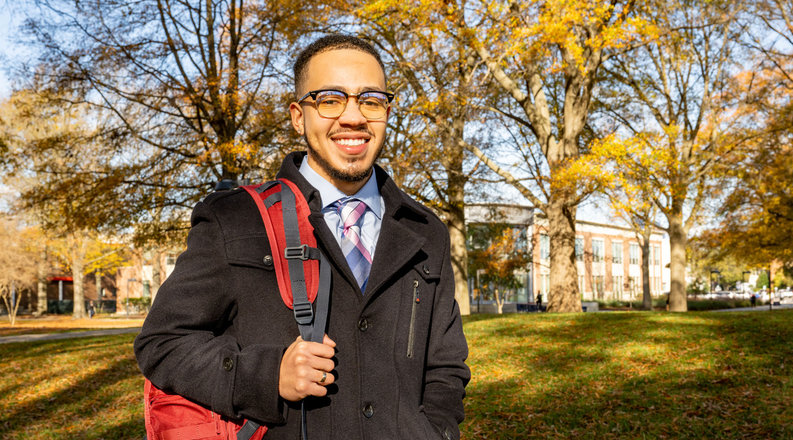 male student posing outside carrying a red backpack