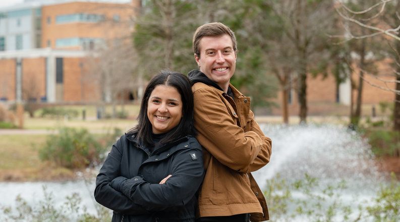 Two students stand back-to-back in front of a building on Old Dominion University’s campus. 