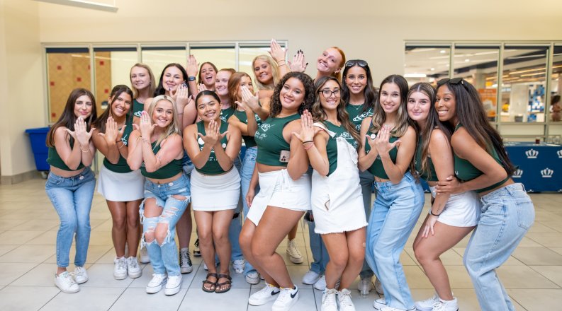 A group of students stand together and make their sorority sign with their hands. 