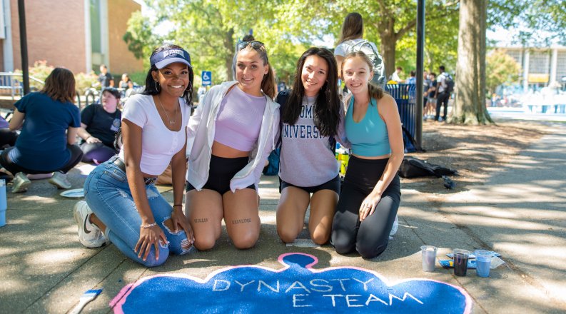 Students kneel in front of a painted crown on a sidewalk. 