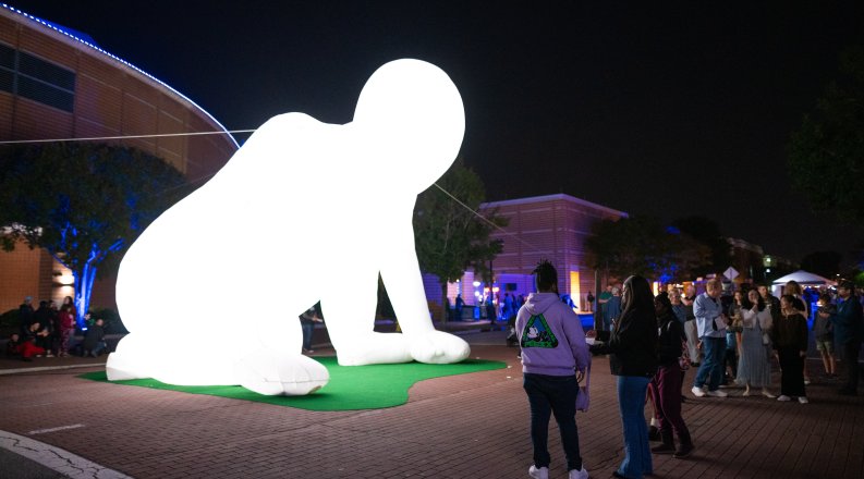 A group of people stand around an illuminated large-scale sculpture of a human figure.