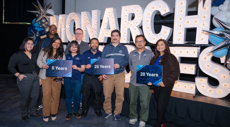 People standing in front of a sign reading "Monarch Milestones" while holding signs.