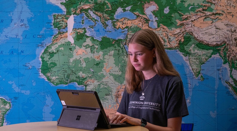 Student on a laptop with a world map behind them