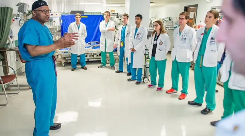 Clad in blue surgical scrubs, Dr Britt stands in a hospital 