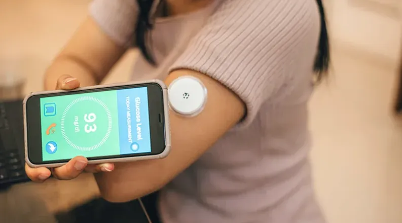 Woman with continuous glucose monitoring on arm and cell pho