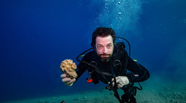 Professor Dan Barshis, Ph.D., holds a piece of coral while scuba divining. 
