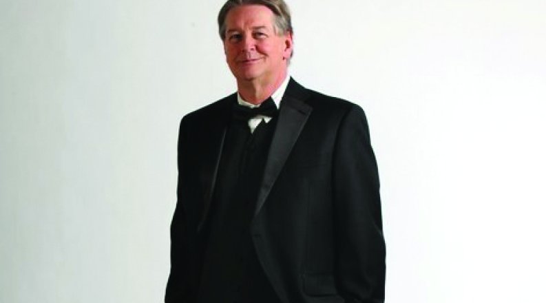 ODU alumnus Eric Feber stands in a white room wearing a tuxedo. 