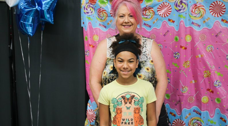 An adult and a child stand smiling in front of a colorful candy-themed backdrop.