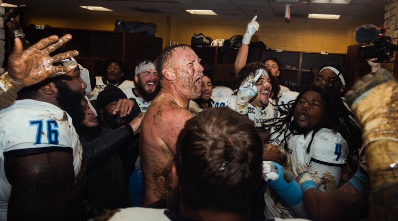 Football players surround muddy coach in locker room