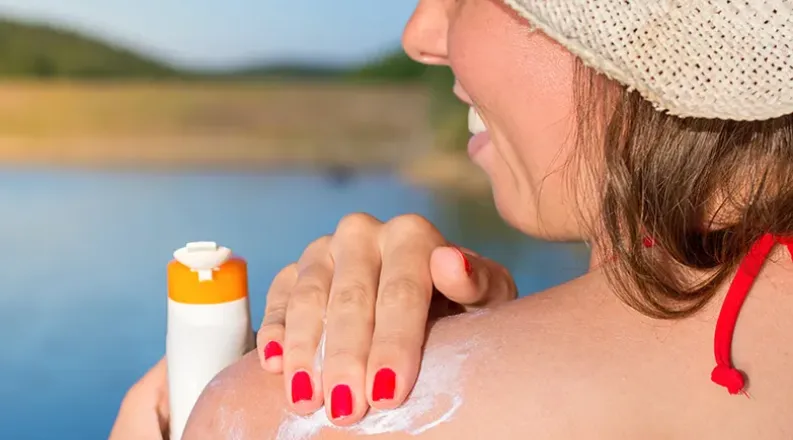 Close up of a woman in a straw hat applying sunscreen on her