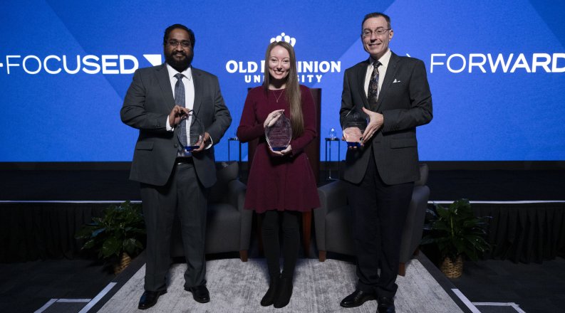 Three people holding awards in front of a screen that reads "forward-focused" 