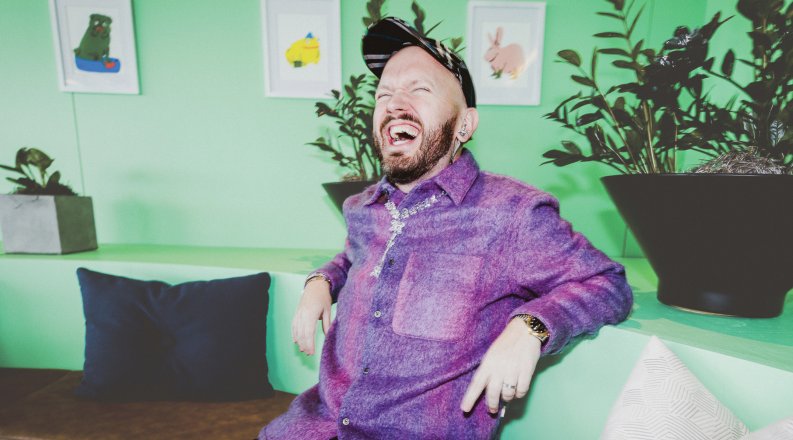 ODU alumnus Nigel Tierney sits on a couch, laughing 