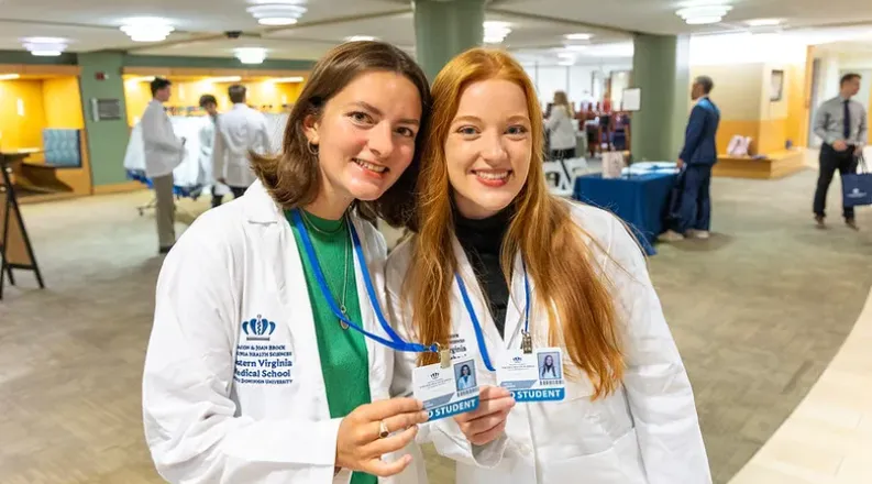Two students smiling in white coats at orientation.