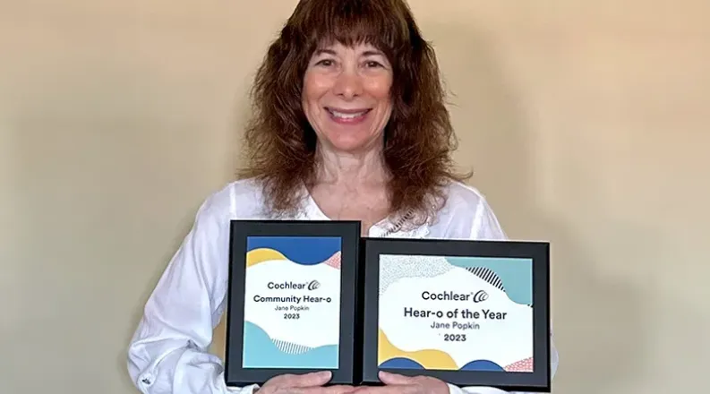 Jane has long curly brown hair, is wearing a white jacket an