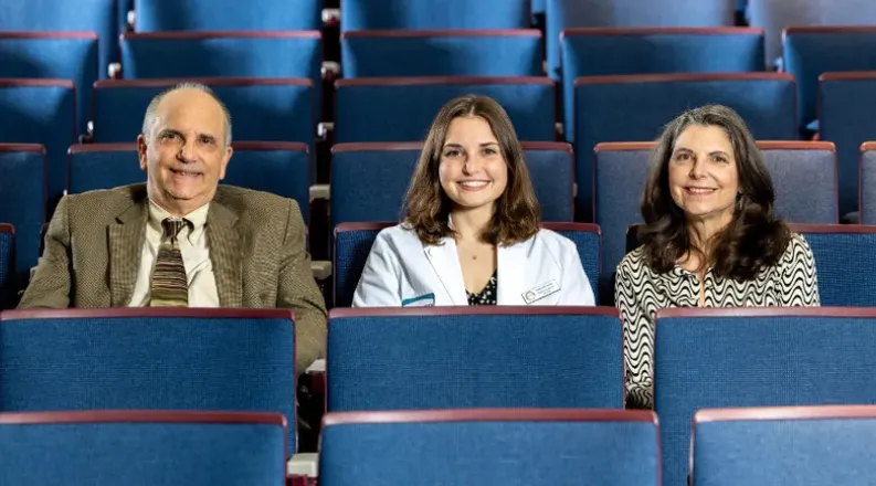 Three individuals smiling while sitting in blue seats in an 