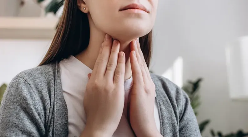 A woman uses both hands to touch her neck. She looks worried