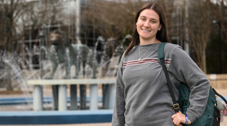 Amie Burdette stands in front of the Old Dominion University lion fountain, holding a backpack and smiling.