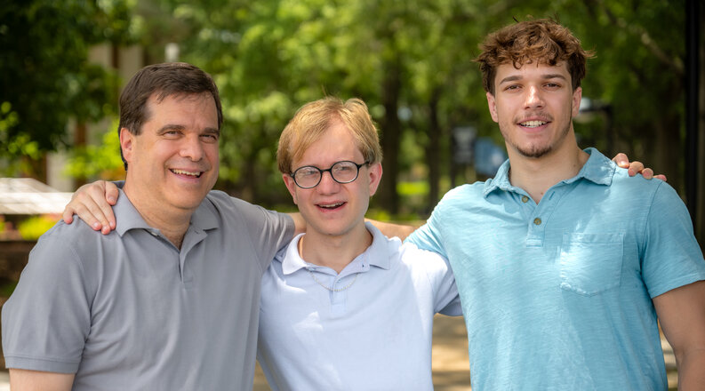 Three smiling men stand with their arms around each other on the Old Dominion University campus. 