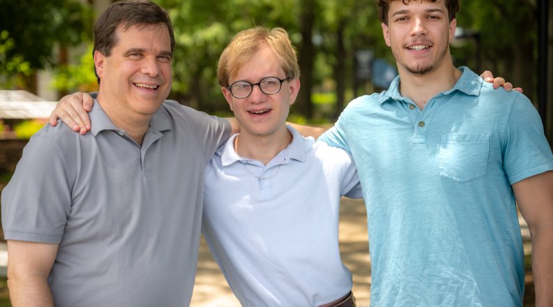 Three smiling men stand with their arms around each other on the Old Dominion University campus. 