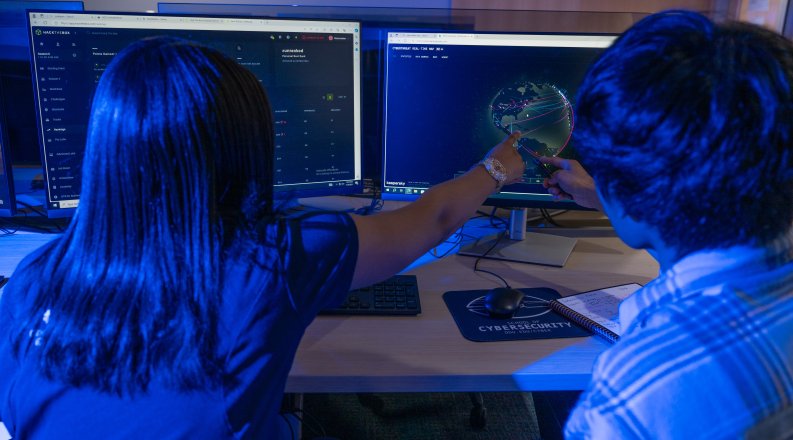 Two people in a dark room looking at computer monitors