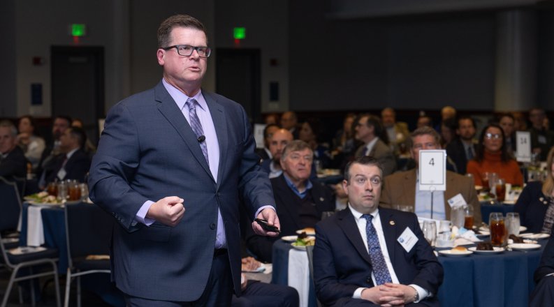 Man in suit talks to an audience seated at tables