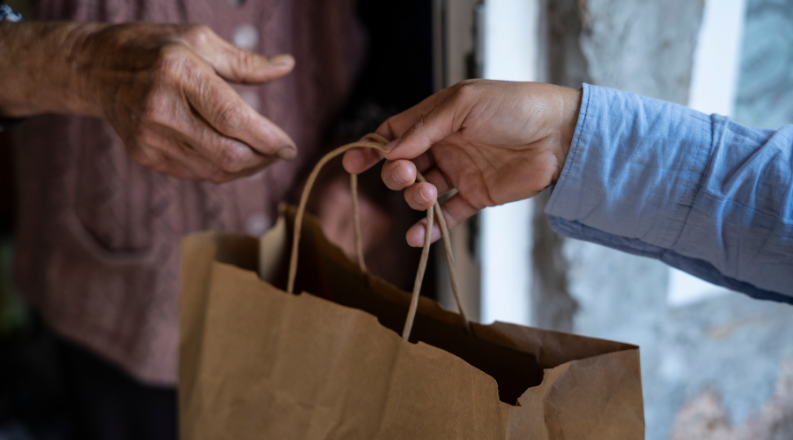 Two hands exchange a paper grocery bag.