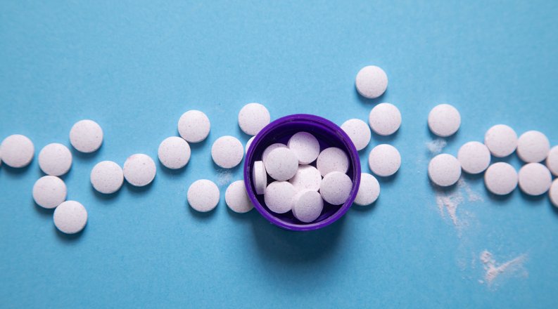 Overhead view of medical pills, both in an open bottle and spread around it.
