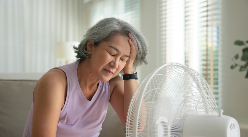 Woman sits on couch with electric fan blowing on her face.