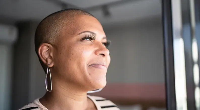 A woman with buzzed hair wearing a striped blouse smiles whi