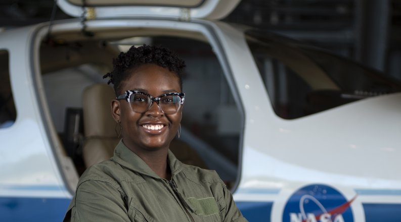 A student in a jumpsuit poses in front of a NASA aircraft.