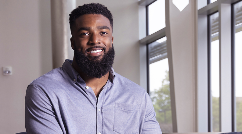A man in a blue shirt poses beside a window.