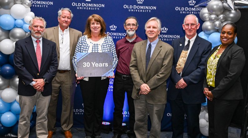 group photo with a sign reading “30 years” in front of a blue backdrop