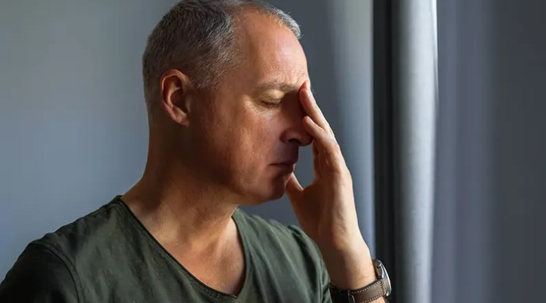 A man with gray hair wearing a gray shirt holds his hand to 