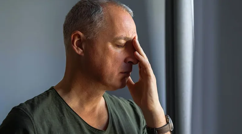 A man with gray hair wearing a gray shirt holds his hand to 