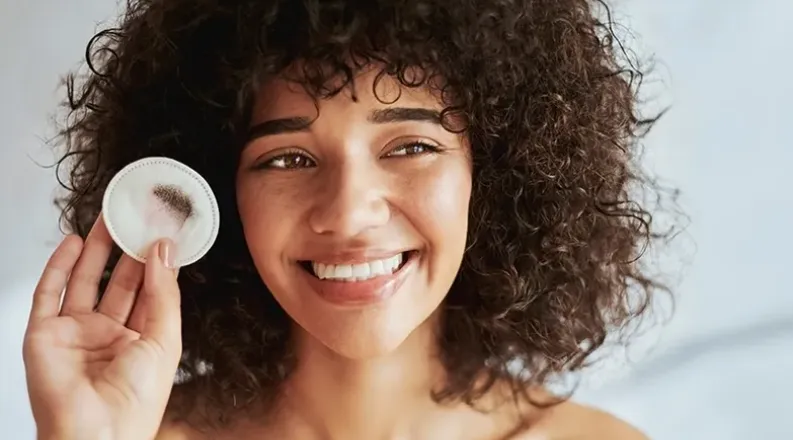 A woman smiles as she removes makeup from her eyes using a c