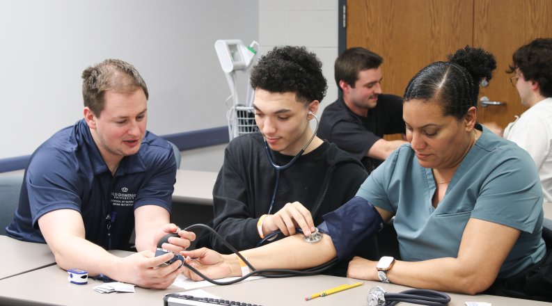 In a classroom, a nursing student is demonstrating how to take blood pressure on a patient.