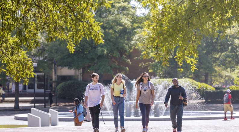 A group of students walk on ODU's campus in front of the lion fountain. 