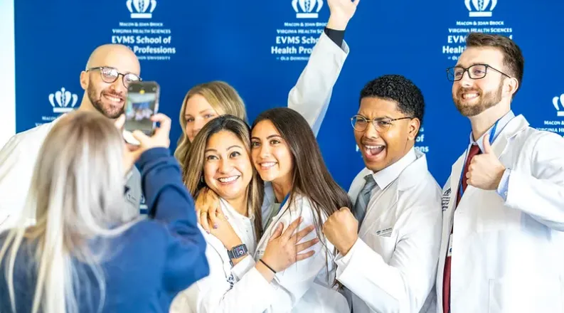 Students in white lab coats smiling as they have their photo