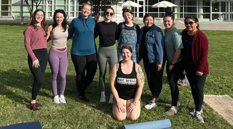 a group of individuals stand smiling together with yoga mats