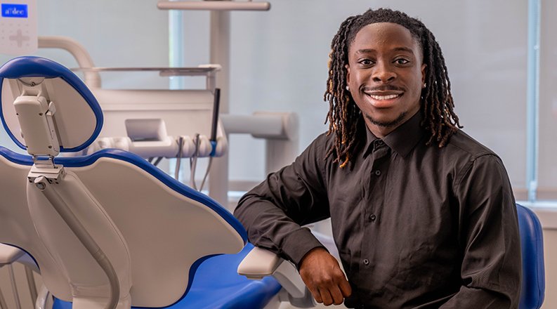 Benjamin Quansah sits next to dental chair in clinic.