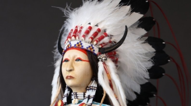 A doll wears traditional Native American dress, including a beaded headdress.