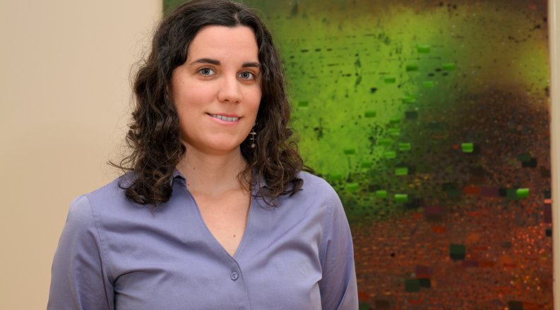 A woman poses for a photo in front of a piece of art. 