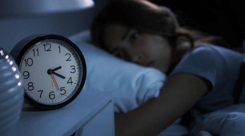 A woman who can't sleep stares at a clock in the middle of the night.