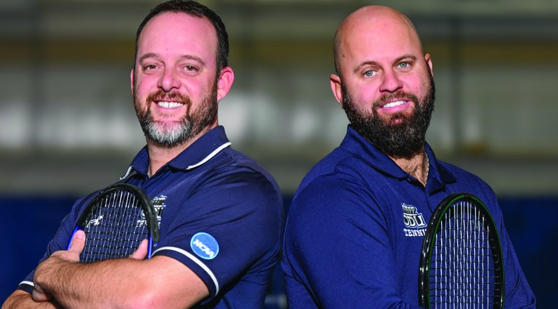 ODU tennis coaches Dominic Manilla and Dominik Mueller stand back-to-back on a tennis court. 